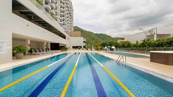 A swimming pool with clear lane markings, adjacent to a modern building with balconies.