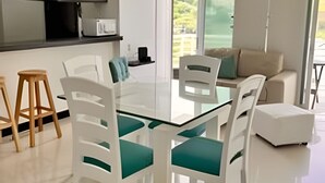Et moderne køkken med hvide skabe, indbygget mikrobølgeovn og et spiseområde med hvide stole og et glasbord.