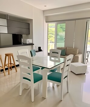 A modern kitchen with white cabinetry, a built-in microwave, and a dining area with white chairs and a glass table. - Rodadero Escape | Pool, Balcony, BBQ & Parking (Santa Marta)