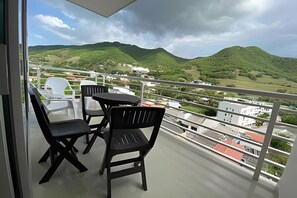A balcony with a table and chairs, overlooking a hilly landscape with buildings in the distance. - Rodadero Escape | Pool, Balcony, BBQ & Parking (Santa Marta)