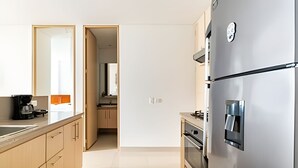 Eine moderne Küche mit einem Edelstahl-Kühlschrank, einer Kaffeemaschine und Blick ins angrenzende Badezimmer.