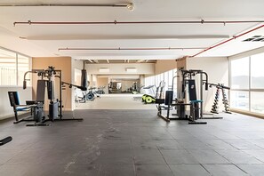 Ein geräumiges Fitnessstudio mit vielfältigen Trainingsgeräten, großen Fenstern und hoher Decke.
