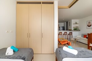 A hotel room with two beds, a wooden wardrobe, a kitchenette, and a dining area with chairs and a table. - Exclusive Ocean View | Playa Salguero • Sky Club (Gaira)