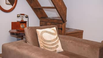 A brown armchair with a decorative pillow, a wooden side table with a rotary phone, and a wooden staircase.