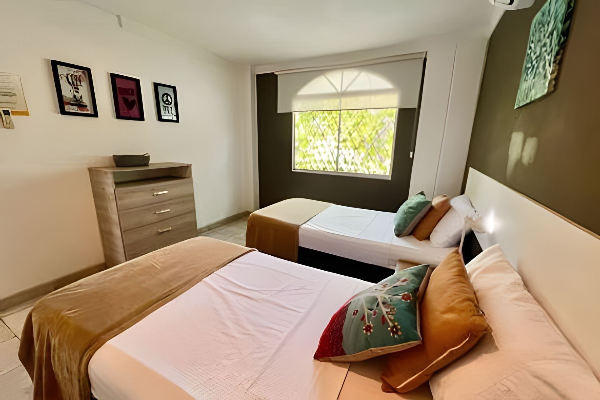 A bedroom with two beds, a dresser, and artwork on the wall.