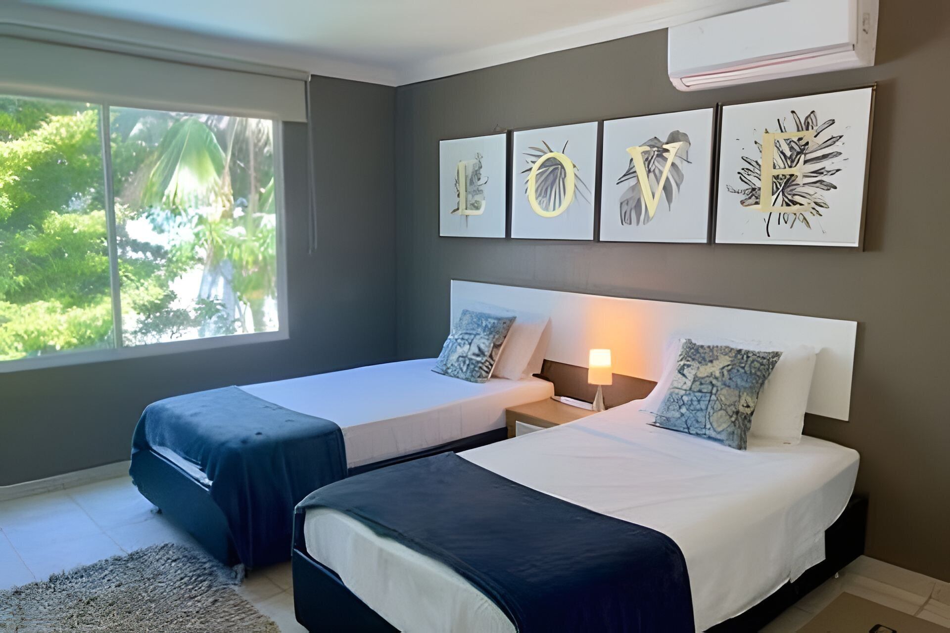 A hotel room with two beds, a nightstand, a lamp, and artwork on the wall.