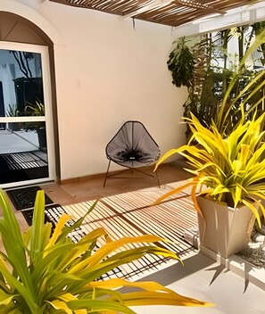 A modern outdoor seating area with a chair, potted plants, and a view of the street. - Lagomar House: Private Pool, BBQ & Beach (Santa Marta)