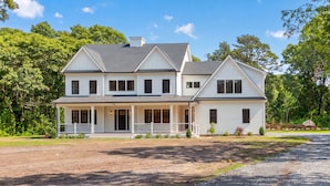 A two-story house with a porch, a driveway, and a well-maintained lawn. - 7BR, 6.5Bath NEW Construction Family Home in Barnstable Village (Barnstable)