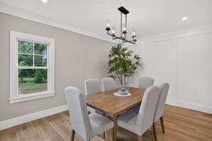 Ein Esszimmer mit Holztisch, sechs grauen Stühlen, einer Pendelleuchte und einem Blumentopf.