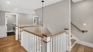 A modern interior with a wooden staircase, white railings, and a light grey wall. - 7BR, 6.5Bath NEW Construction Family Home in Barnstable Village (Barnstable)