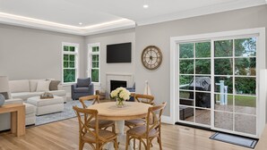 A modern living room with a sofa, armchair, and dining table with chairs. - 7BR, 6.5Bath NEW Construction Family Home in Barnstable Village (Barnstable)