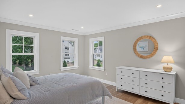 A bedroom with a bed, dresser, and windows with views of a house and trees. - 7BR, 6.5Bath NEW Construction Family Home in Barnstable Village (Barnstable)