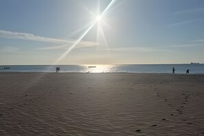 A beach with footprints leading to the water, a boat in the distance, and a clear sky.