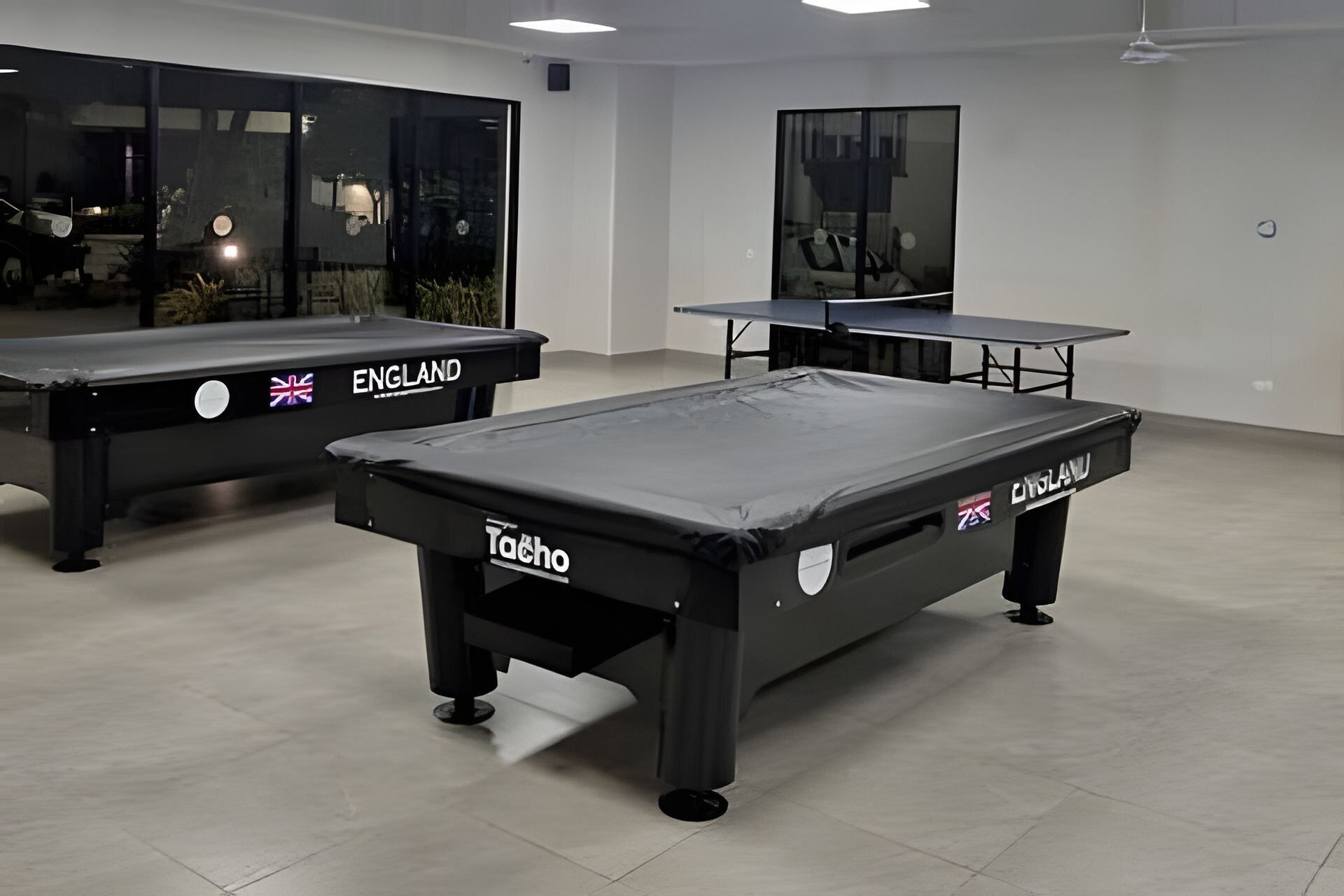 Une salle de billard avec deux tables portant les inscriptions « ANGLETERRE » et « TACHO ».