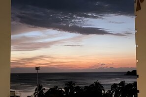 A sunset view from a balcony overlooking the ocean with palm trees in the foreground. - Rodadero: Apt w/ Balcony, Ocean View & Elevator (Santa Marta)