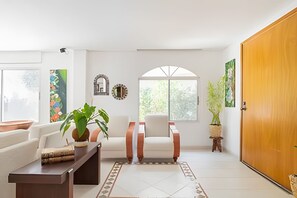 A living room with a white sofa, a wooden coffee table, a potted plant, a chair, and a large wooden door. - Relax: Beach House w/ Private Pool & Sea Access (Santa Marta)