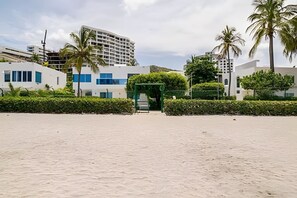 Ein Strandgrundstück mit Sandstrand, modernen Gebäuden und Palmen.