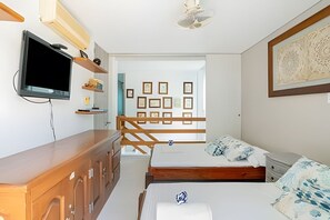 Een slaapkamer met een bed, een aan de muur bevestigde televisie, een houten dressoir en een deur naar een andere kamer.