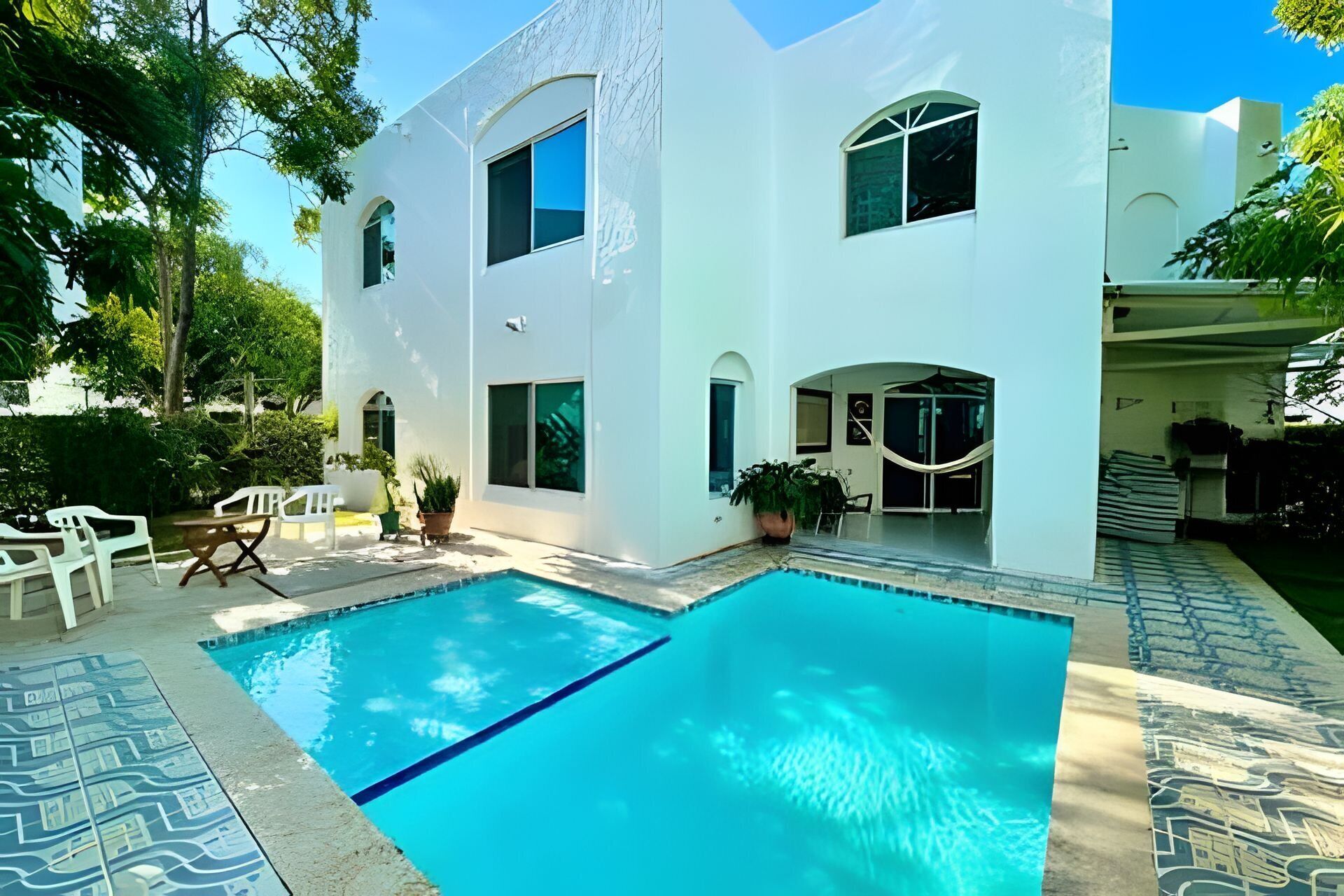 A modern white building with a swimming pool, outdoor seating, and potted plants.