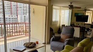 Un salón con sofá, sillones y una mesa de centro. Hay un balcón con vistas a un edificio.