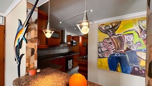 Una cocina con encimera de granito, microondas y lámpara colgante.