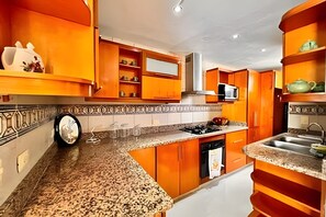 Une cuisine avec des meubles de rangement orange, un four à micro-ondes, une cuisinière et un évier.