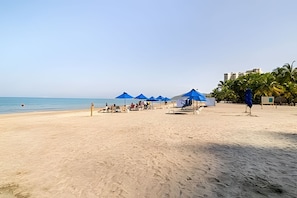A beach with blue umbrellas, a few people, and a peacock statue. - Bello Horizonte: Modern Loft w/ Pool & Beach (Santa Marta)