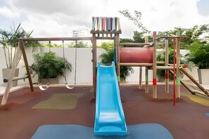 Ein Spielplatz mit einer blauen Rutsche, Klettergerüsten und einem roten, zylindrischen Objekt.