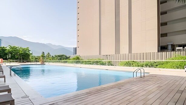 Ein Schwimmbecken mit Holzterrasse, umgeben von einem Gebäude mit flacher Fassade und Blick auf Berge im Hintergrund.
