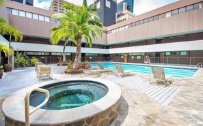 Zona de piscina de hotel con jacuzzi, sillas de descanso y una palmera.