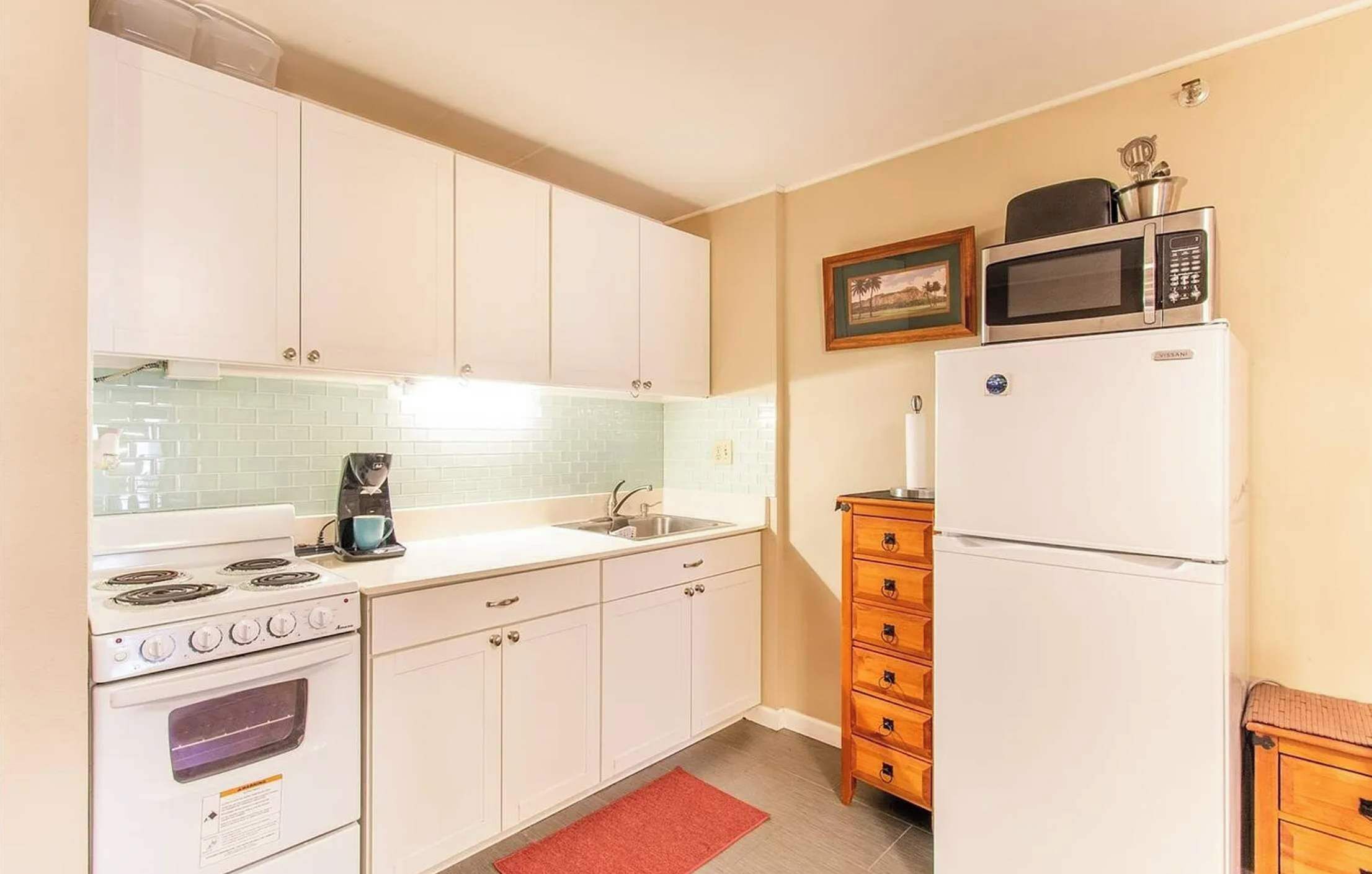 Cocina compacta con armarios blancos, estufa, microondas y refrigerador.
