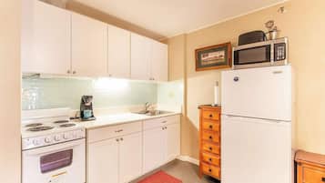 Cocina compacta con armarios blancos, estufa, microondas y refrigerador.