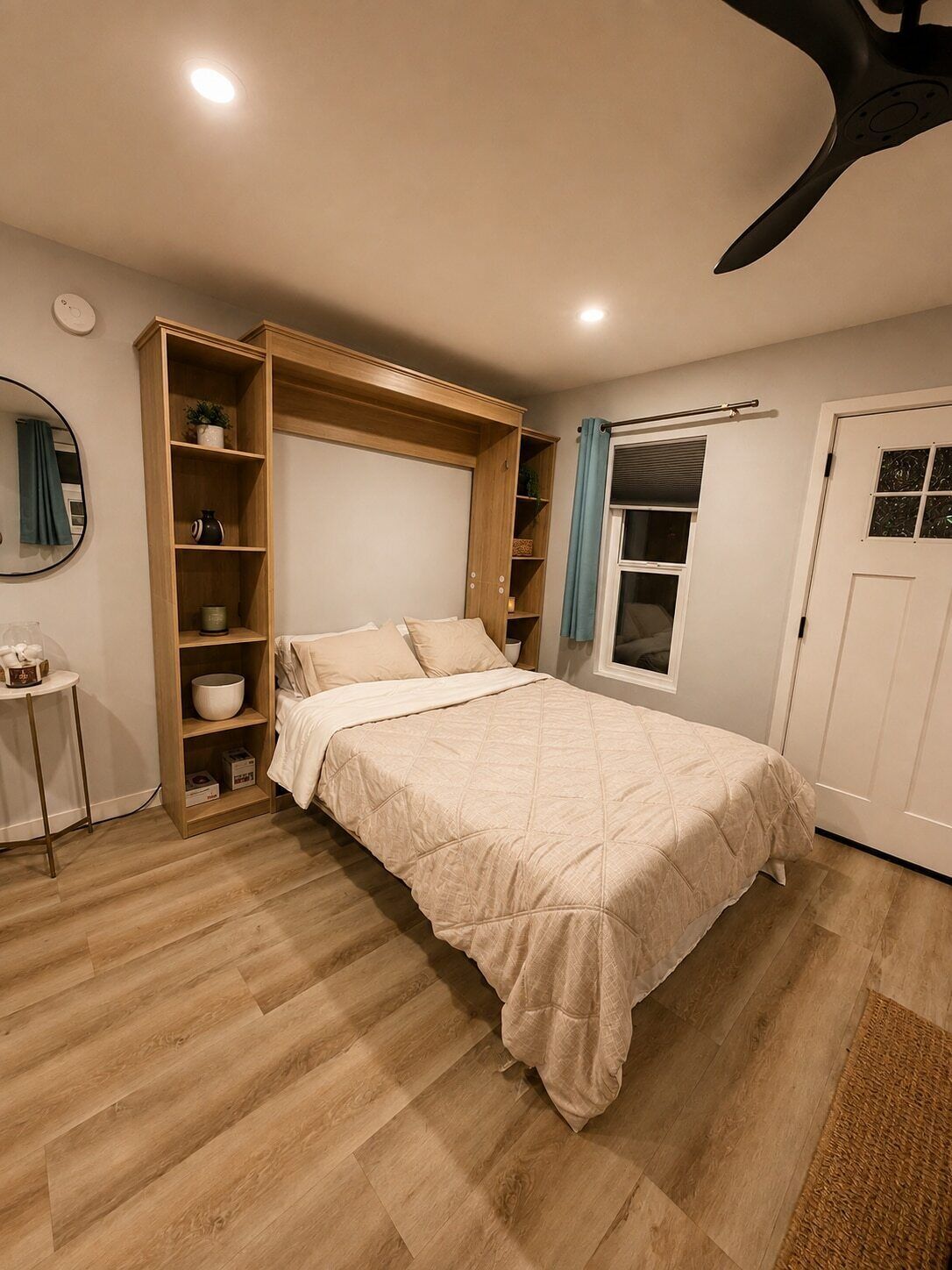 A bedroom with a bed, built-in shelving, a bedside table, and a door with a window.
