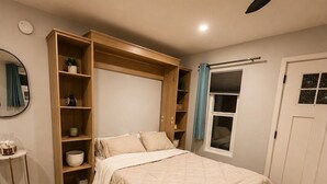 A bedroom with a bed, built-in shelving, a bedside table, and a door with a window. - Private Patio & Fire Pit Near San Diego (Spring Valley)