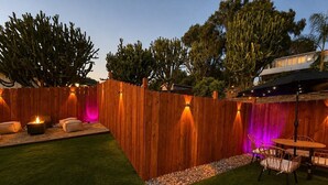 A backyard with a wooden fence, a fire pit, outdoor furniture, and a table. - Private Patio & Fire Pit Near San Diego (Spring Valley)
