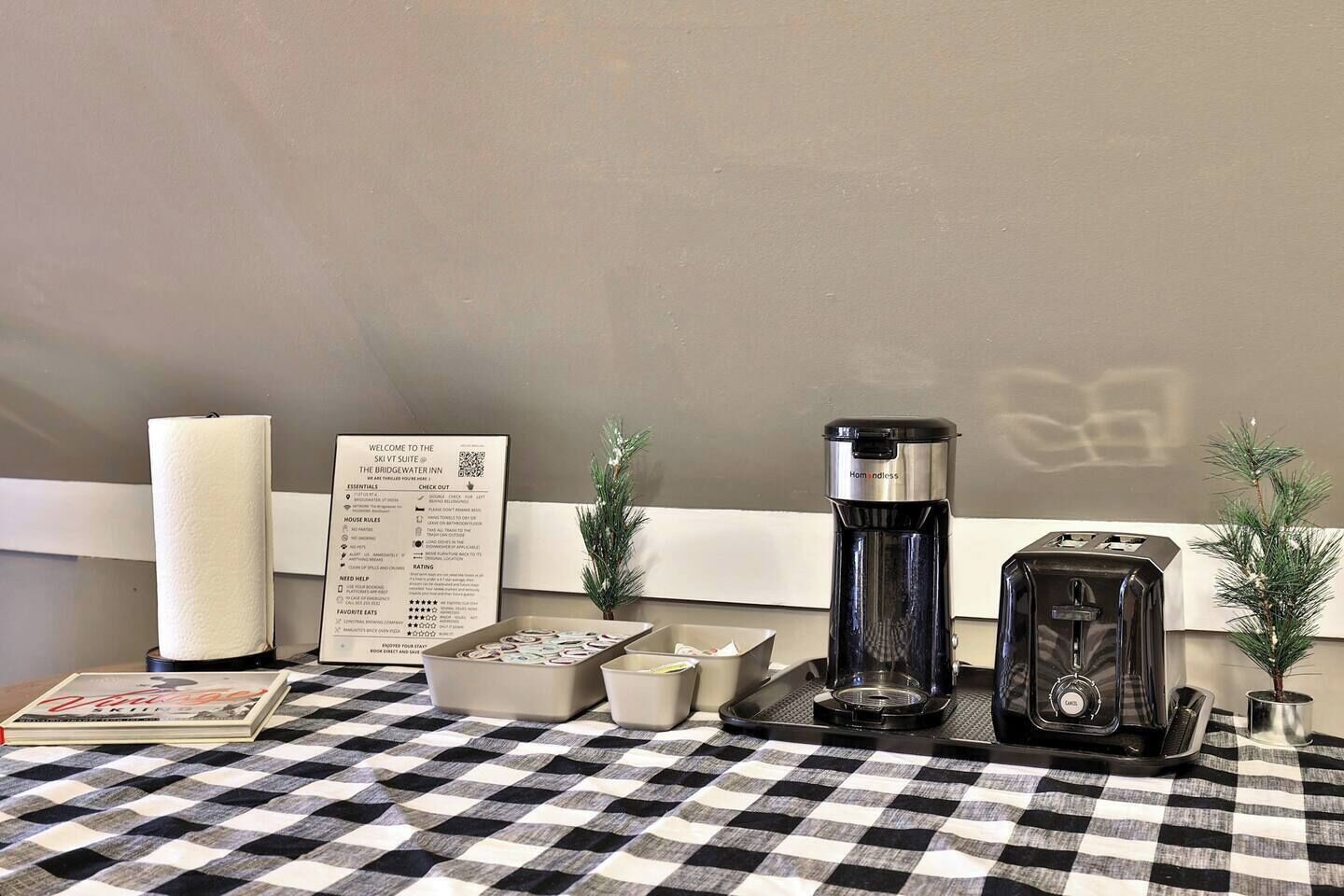 Ein Check-in-Bereich mit Schilder für Check-out, einer Speisekarte, einer Kaffeemaschine, einem Toaster und einer kleinen Weihnachtstanne.