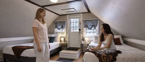 A bedroom with two beds, a door, and a small table with a lamp.