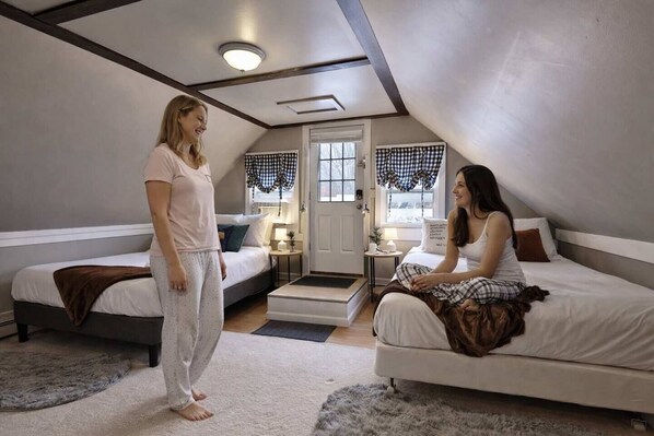 A bedroom with two beds, a door, and a small table with a lamp.