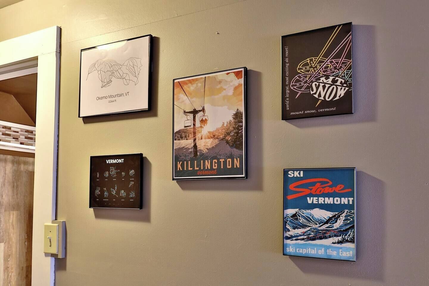 En væg med fire indrammede ting: et kort over Vermont, en plakat af Killington, en plakat med sne, og en plakat af Ski Vermont.