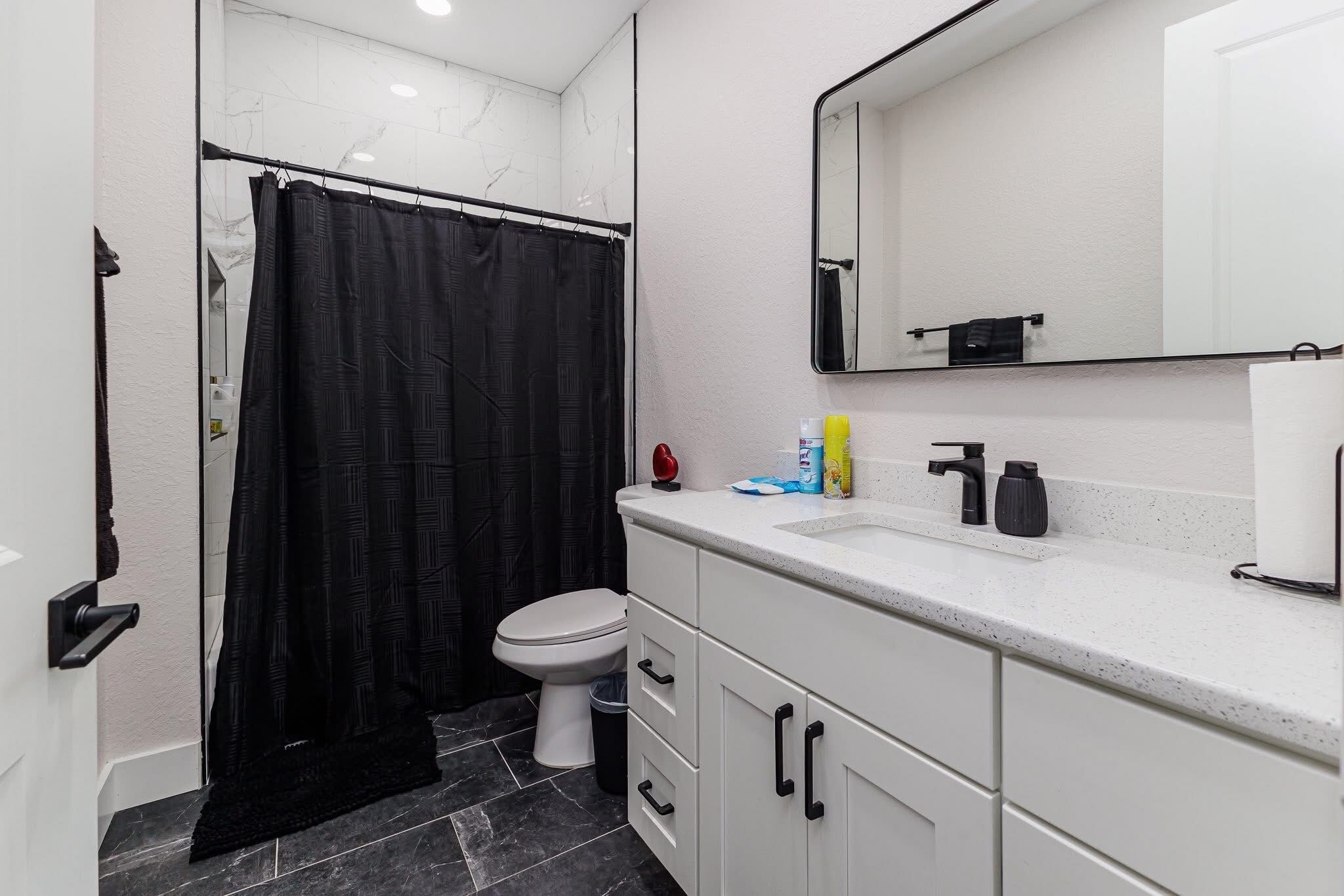 A bathroom with a toilet, a sink, a mirror, and a shower curtain.