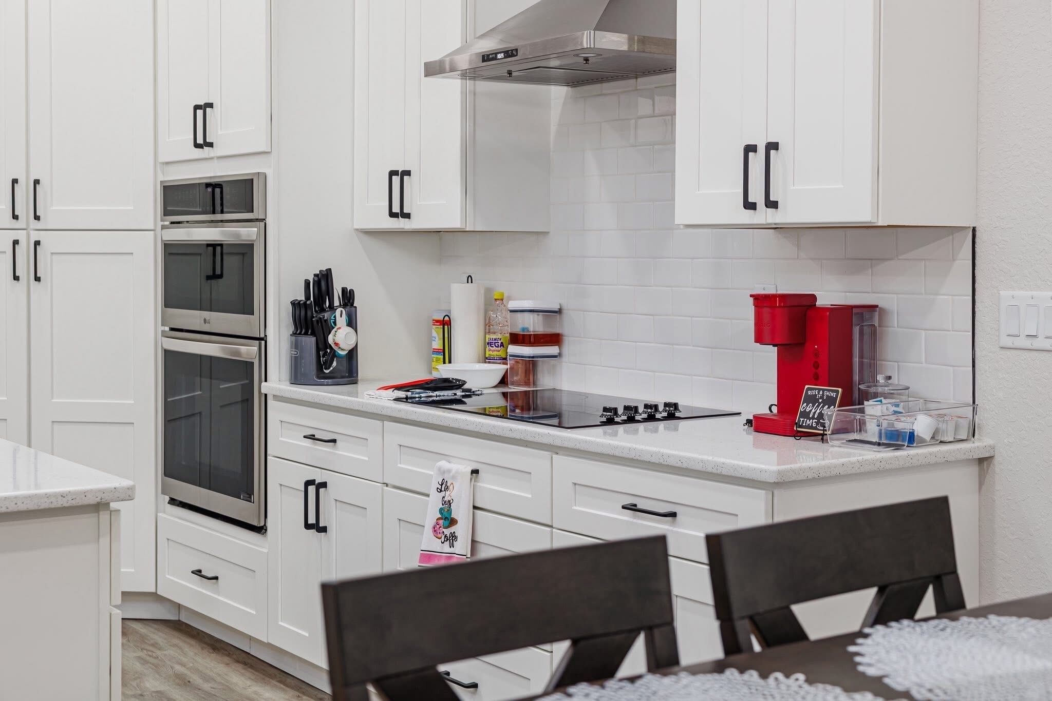 A modern kitchen with white cabinets, stainless steel appliances, and a coffee machine.