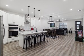 A modern kitchen with white cabinets, a central island with bar stools, and a dining area with a black sofa and chairs. - Luxury 2-Bedroom Apartment / Duplex Shared Living Bartow near Lakeland LEGOLAND (Bartow)