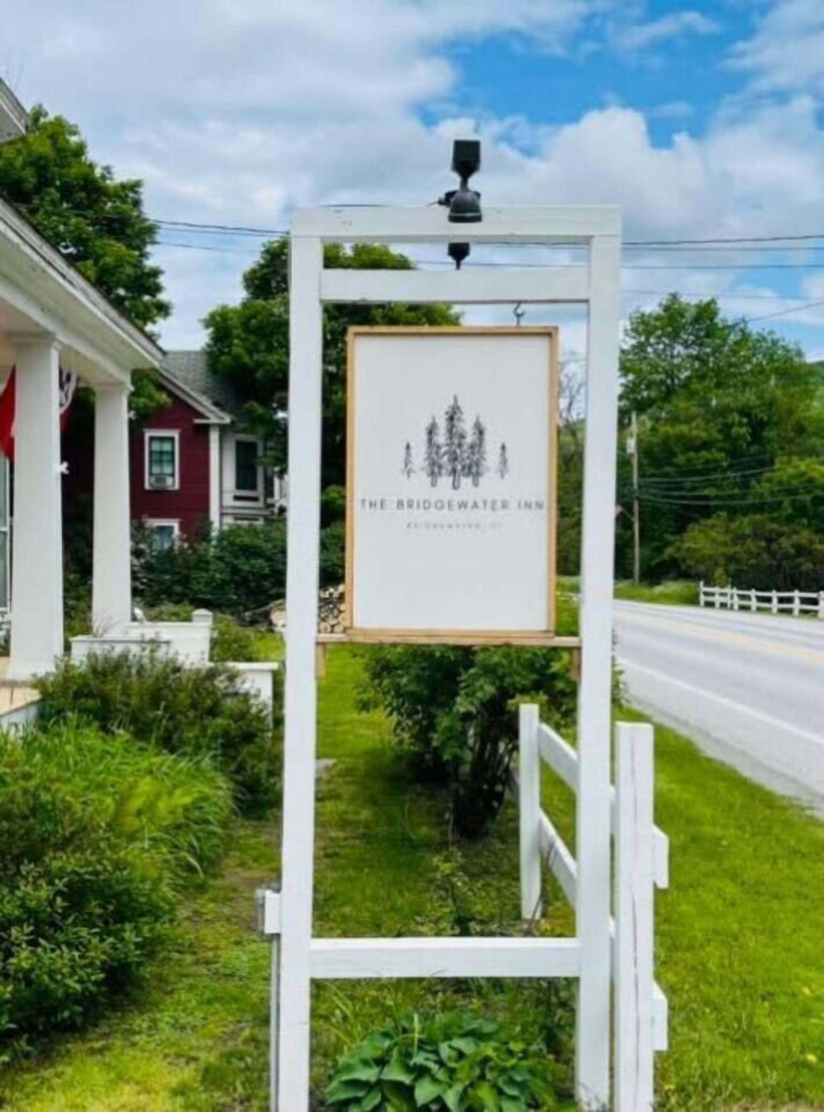 A signboard for The Bridgewater Inn with a simple design, located beside a road with a white fence and greenery.
