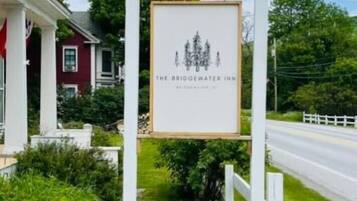 A signboard for The Bridgewater Inn with a simple design, located beside a road with a white fence and greenery.