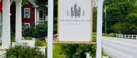 A signboard for The Bridgewater Inn with a simple design, located beside a road with a white fence and greenery.