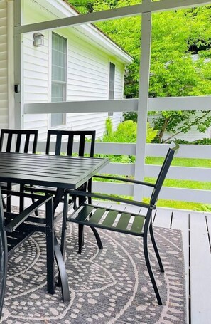 Une terrasse couverte avec une table et des chaises, un tapis à motifs et une vue sur une maison blanche et de la verdure.