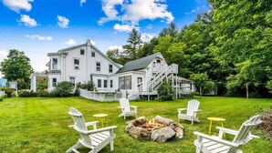 A large white house with a fire pit in the center surrounded by Adirondack chairs. - Bridgewater Living - Woodstock Suite (Bridgewater)