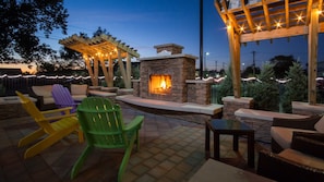 Un patio al aire libre con chimenea de piedra, pérgola de madera y sillas Adirondack de colores.