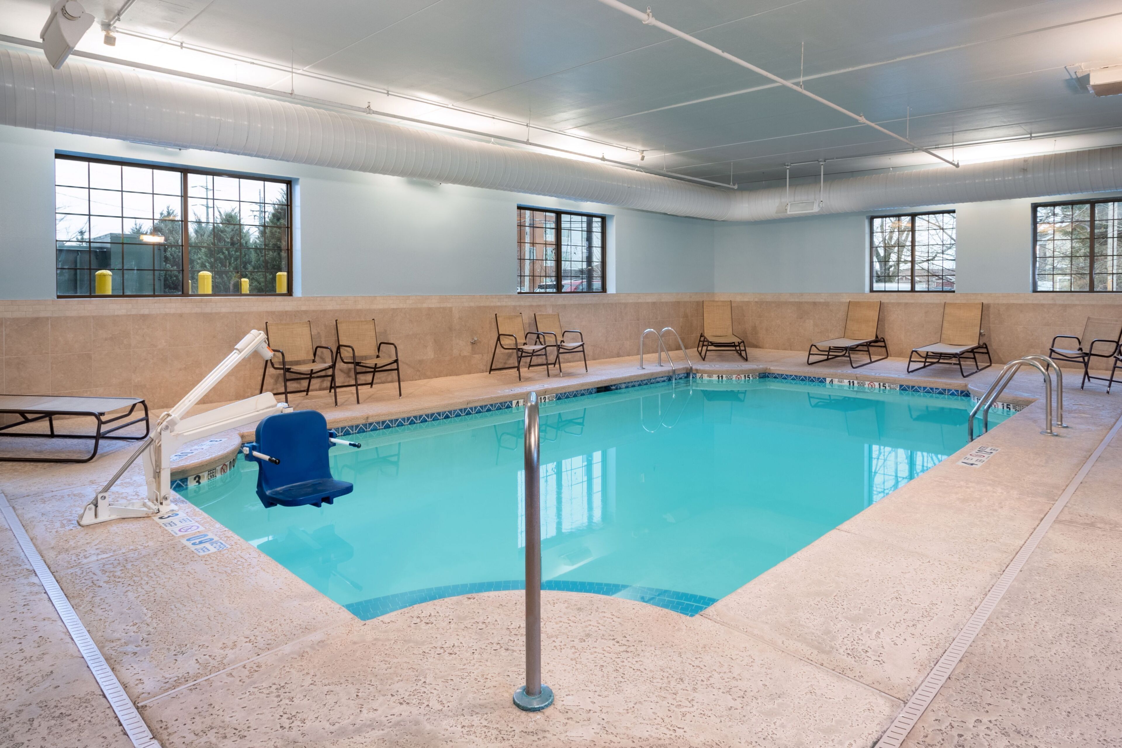An indoor swimming pool with clear water, surrounded by lounge chairs, and large windows providing natural light.