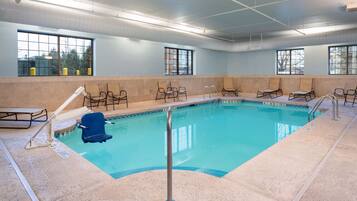 An indoor swimming pool with clear water, surrounded by lounge chairs, and large windows providing natural light.